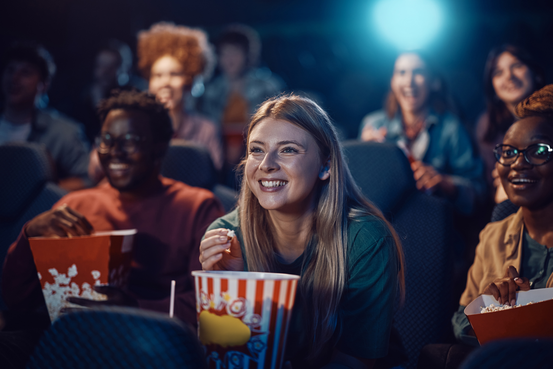 Happy woman eating popcorn during movie premiere in a theatre.