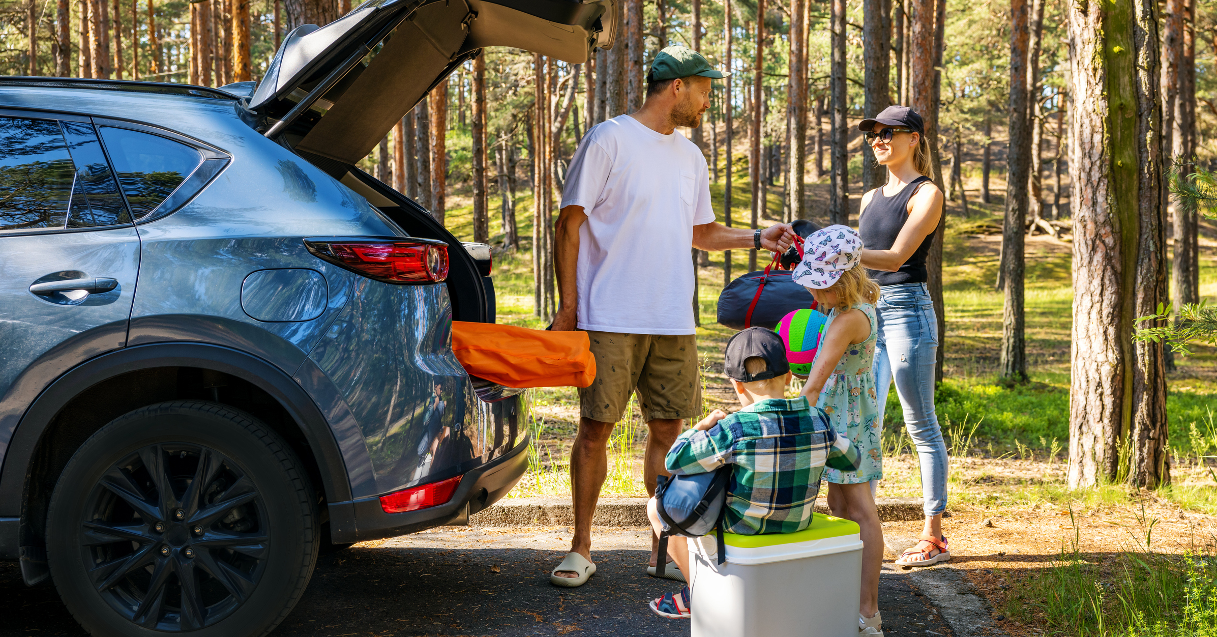 family with kids remove the camping supplies from car trunk at forest. summer holidays, road trip
