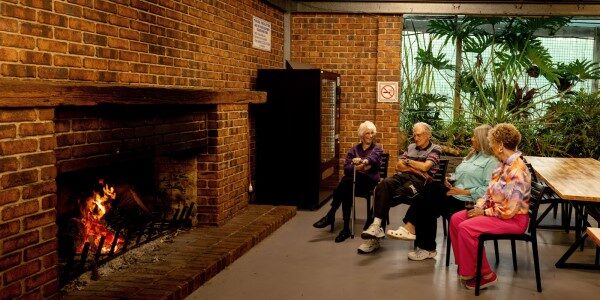 A group of people gathered around a fire in a room at Normanville Park Communal Fire, enjoying warmth and conversation.