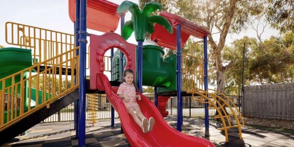 A child joyfully playing on a slide at the Normanville Park playground, surrounded by colorful play equipment.